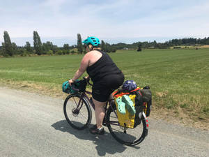 騎單車者在鄉村碎石路上騎著載滿行李的旅行單車穿過綠色田野