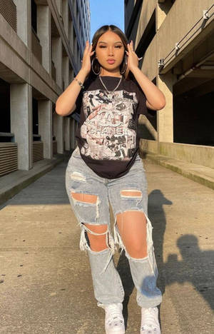 年輕女性穿著破洞牛仔褲和圖案T恤在城市小巷中擺姿勢。