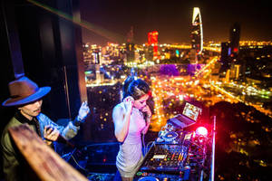兩位DJ在屋頂上表演，俯瞰充滿活力的夜景城市景觀。