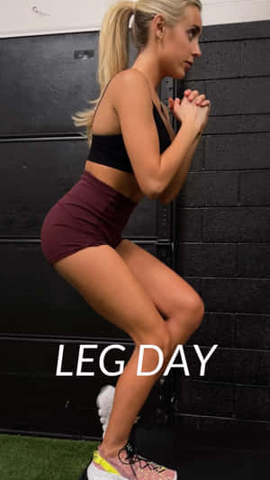 金髮女子在健身房做深蹲，黑色磚牆上寫著『LEG DAY』。 — 健身 壁紙