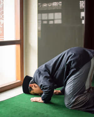 男子在清真寺窗邊的綠色地毯上祈禱