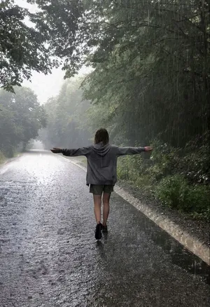 一個人在下雨的森林小路上張開雙臂行走。