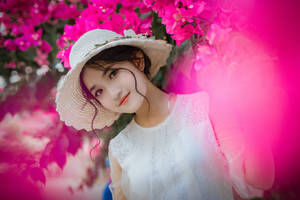 身穿白色連衣裙和草帽的年輕女子在粉紅色花朵下微笑。 — 唯美花朵動圖 壁紙