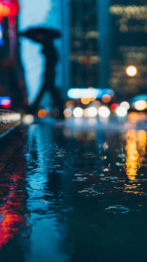 撐著雨傘的行人剪影在夜晚雨中城市行走，伴隨著發光的燈光反射。 — 雨 壁紙