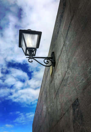 復古街燈固定在石牆上，藍天白雲下