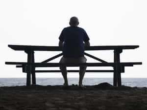 一個男人獨自坐在野餐桌旁，在黃昏時面向海洋。
