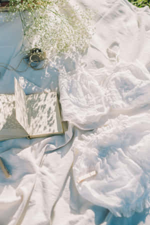 白色布料、打開的書、花朵和蕾絲內衣在明亮陽光下。 — 美學 壁紙