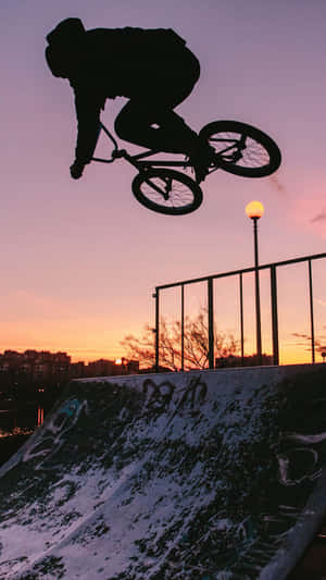 BMX車手在日落時分在塗鴉坡道上空以剪影表演特技。