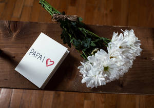 寫有「PAPAI」和心形的便條，旁邊有白色花，在木上。