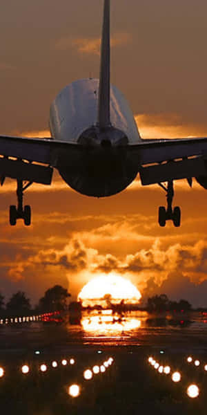 飛機在日落時降落，帶有跑道燈光和橙色天空 — 18:9 壁紙