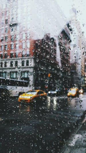 窗戶上的雨滴，可看到有黃色的士和磚砌建築的城市街道景色。