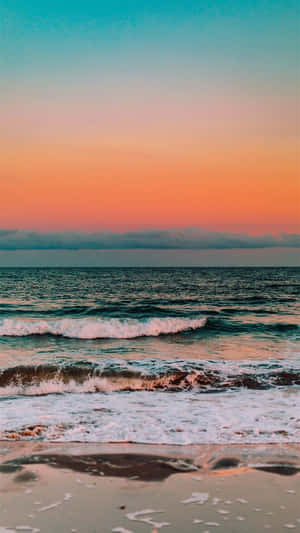 日落時分的海浪在濕沙上反射出橙、粉紅和藍綠色的天空。