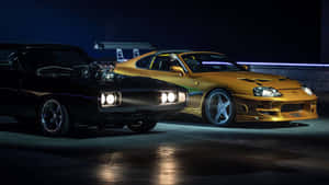 兩輛經典肌肉車，黑色道奇Charger和金色豐田Supra，夜間並排停放，車頭燈亮著。