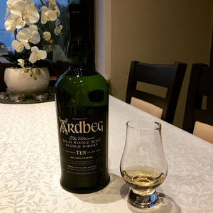 一瓶Ardbeg威士忌和品酒杯放在圖案桌布上，配有白色蘭花。