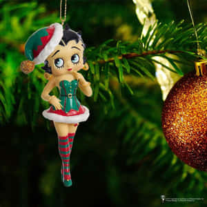 Betty Boop 聖誕裝飾掛在松樹上，旁邊有一個金色聖誕球。