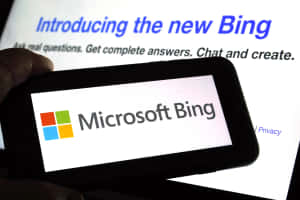 手拿著顯示Microsoft Bing標誌的電話，背景有筆記型電腦。