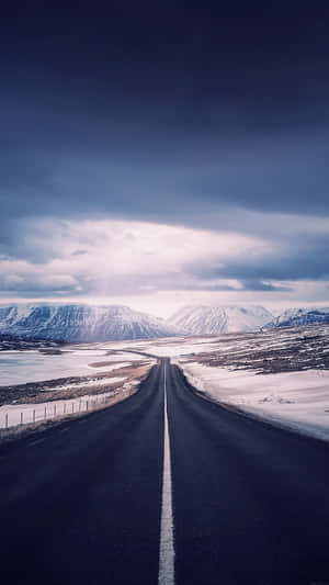 在多雲的天空下，一條長而直的道路穿過積雪的山脈。