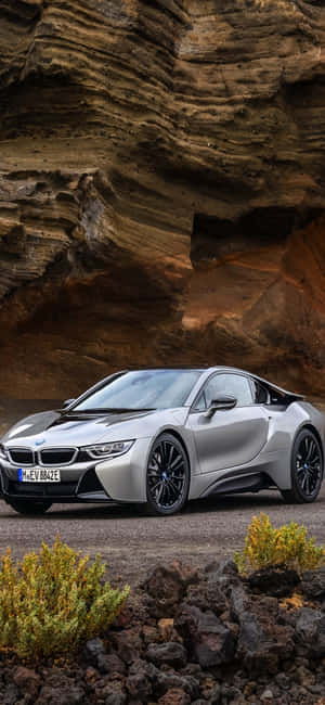銀色BMW i8跑車停泊在岩石懸崖下，伴有沙漠灌木。 — Redmi Note 壁紙