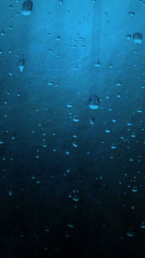 夜晚刮花玻璃窗上的藍色雨滴