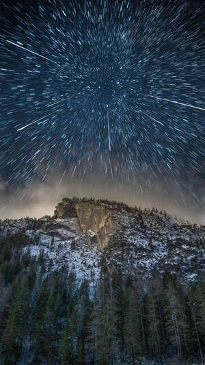 夜間白雪覆蓋的山峰和松樹林上方的星軌。