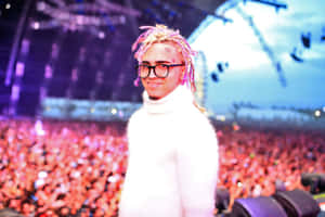 戴著彩色辮子和眼鏡的男人在音樂會上微笑，身後有大量人群。