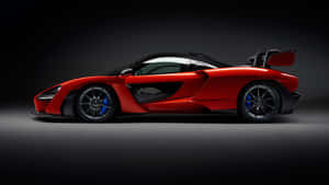 在攝影棚燈光下，帶有黑色飾件和藍色制動器的紅色McLaren Senna跑車。