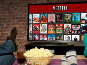 雙腳抬起，前面有爆米花和汽水，電視顯示Netflix。