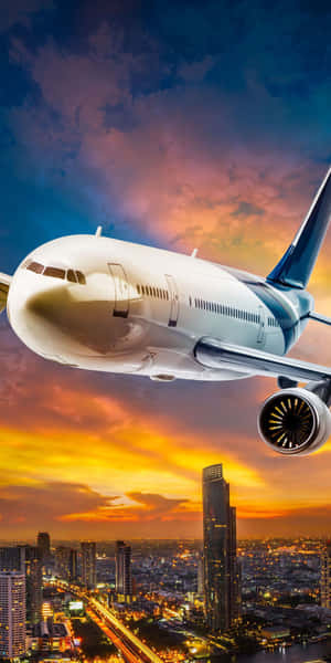 客機在日落時分飛越城市，建築物發光，天空橙色。 — 18:9 壁紙