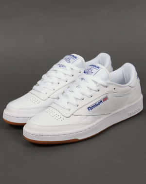 灰色背景上的白色Reebok Classic運動鞋，帶有藍色標誌和橡膠鞋底。 — 4:5 壁紙