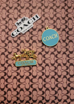 三個Coach品牌別針在標誌性圖案皮革背景上。