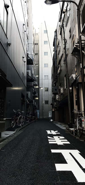 狹窄的城市小巷，有高樓大廈和日本道路標記。 — Pixel 7a 壁紙