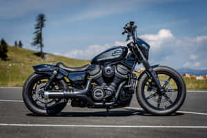 啞光黑色Harley-Davidson電單車停在鋪砌道路上，背景有山丘和天空。 — 哈雷戴維森 壁紙
