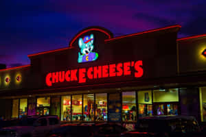 夜間亮燈的 Chuck E Cheese's 遊戲機中心建築，外面停有汽車。