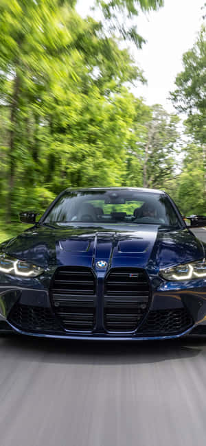 藍色BMW M3在森林中疾馳，背景有模糊的綠色樹木和道路。 — Pixel 7 Pro 壁紙