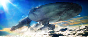 一艘大型未來派太空船在雲層上方飛行，天空中有明亮的太陽。 — 銀河 壁紙