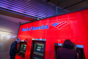 兩個喺紅色牆壁同紫色天花板燈光嘅Bank of America分行內使用自動櫃員機嘅人。