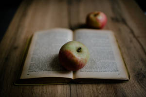 一個紅色和綠色的蘋果放在木桌上的打開書本上。