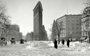 白雪覆蓋的城市街道，熨斗大廈附近有行人與馬車。