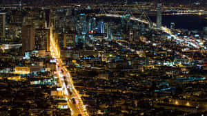 繁華城市的夜間鳥瞰圖，有燈火通明的建築物和一座橫跨水面的燈光橋樑。
