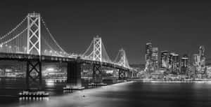 夜間城市景觀，燈光璀璨的海灣大橋和摩天大樓倒映在水中。