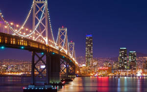 海灣大橋與城市天際線在夜間亮燈，水面倒影。