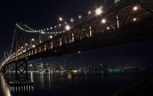 夜間背景中城市燈光映襯下，一座燈火通明的吊橋橫跨水面。