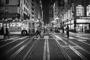 夜間城市街道，無軌電車和行人在高樓大廈之間橫過路軌。