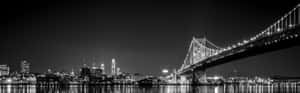 海灣大橋和三藩市天際線的黑白夜景，城市燈光倒映在水面上。