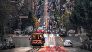 纜車在舊金山陡峭的街道上爬升，旁邊有汽車和樹木。
