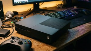 黑色Xbox One主機和手掣在木桌上，配有發光鍵盤和顯示器