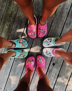 五個人穿著帶有貼紙的彩色Crocs，在木甲板上圍成一個圓圈站立。