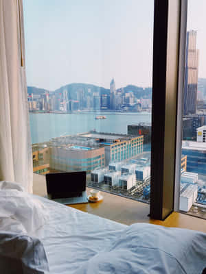 未整理的床鋪，窗邊放著手提電腦和咖啡，俯瞰香港天際線。 — iPad Pro 12.9 壁紙