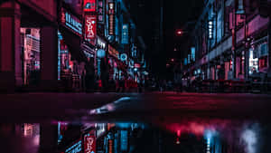 霓虹招牌倒映在繁忙城市街道的雨水坑中，夜晚時分。 — 寬螢幕 壁紙