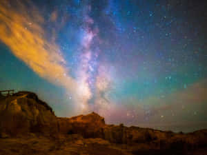 銀河系在星空下閃耀於岩石懸崖之上，伴隨著橙色雲朵。